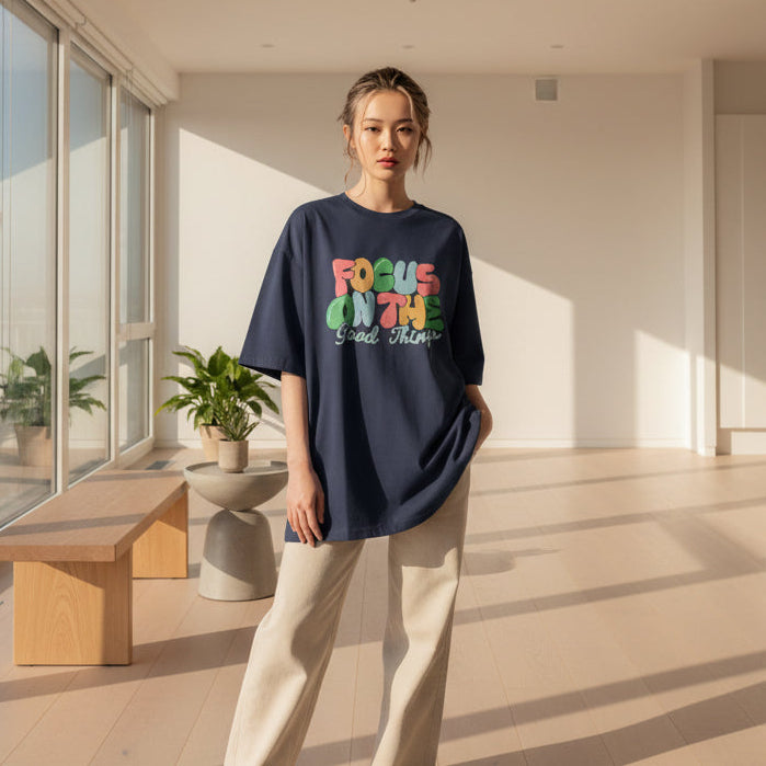 A person wearing a navy-colored oversized t-shirt with the text 'FOCUS ON THE Good Things' printed on the front.